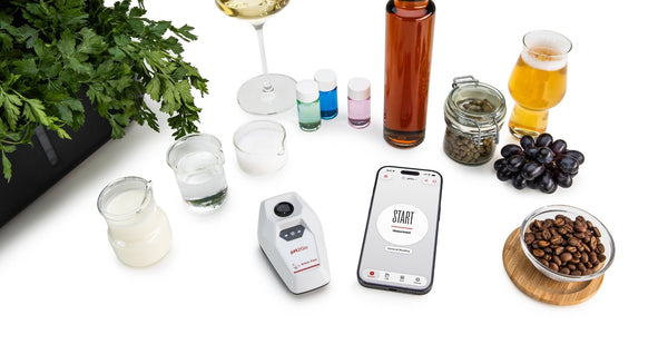 pH2Go and Smartphone with Lab Meister App on a table setup with yoghurt, water, salt, pH buffers, vinegar, wine, hop, grapes, beer, coffee beans and parsley in a grower all around the devices