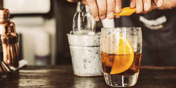 Bartender crafting a cocktail with an orange twist, indicative of the spirit analysis possible with the EasyDens by Anton Paar Digital Density Meter for Spirits.