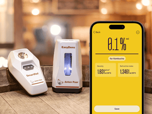 Smartphone showcasing Kombucha density and refractive index measurements next to EasyDens by Anton Paar Digital Density Meter and SmartRef Digital Refractometer.